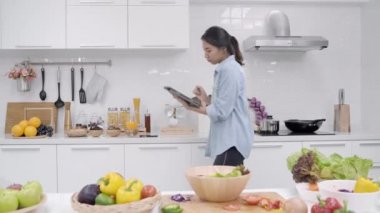 Mutlu Asyalı kadın mutfakta kadın kullanım evde sağlıklı yemek için organik sebze yemek yaparken seyir tarifini tablet kullanma. Yaşam tarzı kadın gıda kavramı yapma.
