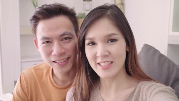 亚洲夫妇使用智能手机视频电话与朋友在客厅在家里 甜蜜的夫妇享受爱的时刻 而躺在沙发上放松在家里 生活方式夫妇在家里放松的概念 — 图库视频影像
