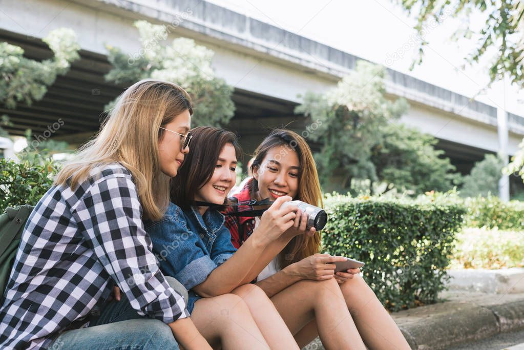 Group of Asian women sitting together and looking checking photo while traveling at park in urban city in Bangkok, Thailand. Lifestyle friends tourist travel holiday in Thailand concept.