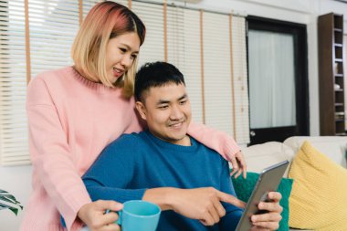 Çekici Asya tatlı çift kanepede yatan tablet kullanma ne zaman onların evde oturma odasında rahatlayın. Koca ve karısı kullanarak dinlenmek ve romantik zaman ev concept.