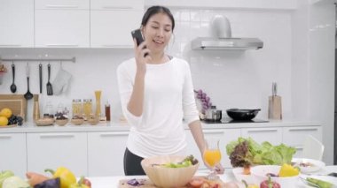 Salata sağlıklı yemek yapma ve smartphone mutfakta güzel kadın kullanımı organik sebze salatası evde hazırlamak konuşurken Genç Asyalı kadın. Yaşam tarzı kadın evde kavramı relax.