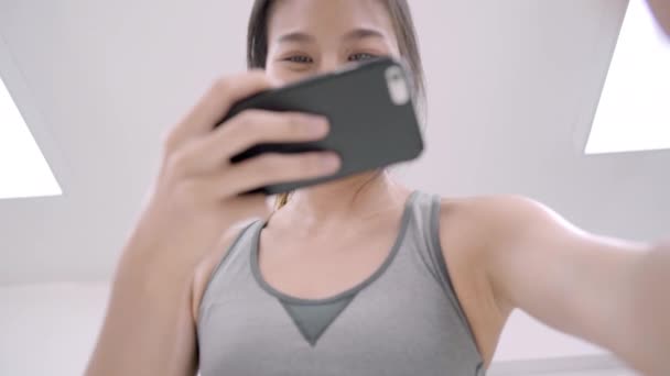 年轻的亚洲博主女性在厨房的社交媒体上使用智能手机图片帖 女性在家里做运动服装做沙拉 生活方式的女性放松在家里的概念 — 图库视频影像