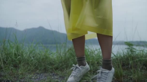 慢动作 年轻的亚洲女子穿着雨衣站在湖边玩雨 感觉很开心 生活方式的女性在雨天享受和放松 — 图库视频影像