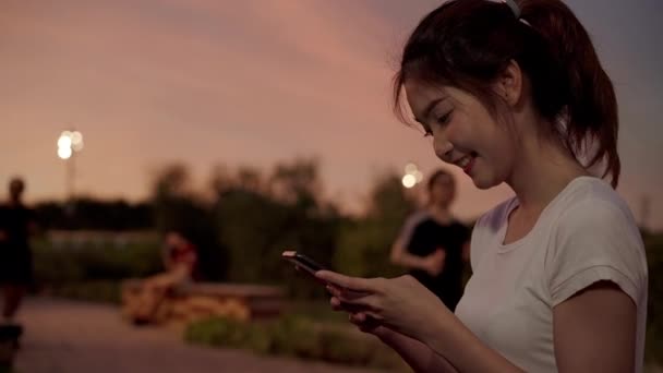 陽気なアジア観光ブロガーの女性が夜の繁華街で路上を歩きながらスマート フォンでタッチ スクリーン技術を使用して ライフ スタイル バックパック観光旅行休暇の概念 — ストック動画