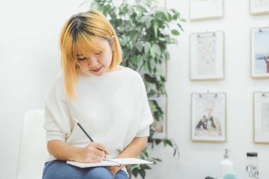 Asyalı kadın yazma alışveriş mutfak tezgahı evde ve okuma kalem tarafından Not Defteri'nde listeler ve alışverişe için tüm malzemeyi hatırlamaya çalışır. Yaşam tarzı kadın evde kavramı relax.