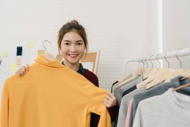 Asyalı kadın moda çalışma, kontrol ve moda stüdyoda çalışırken raf kıyafet tasarımı giysiler seçerek Tasarımcısı. Yaşam tarzı güzel profesyonel tasarımcı kadın kavramı çalışma.