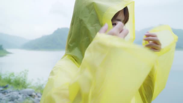 年轻的亚洲女人穿着雨衣站在湖边玩雨时感到很高兴 生活方式的女性在雨天享受和放松 — 图库视频影像