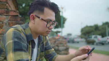 Yavaş hareket - Seyahat Asya adam kontrol süre sosyal medya Ayutthaya, Tayland tatil gezisi geçirdikten sonra rahatla, erkek zevk yolculuğu geleneksel şehirde inanılmaz Simgesel Yapı itibariyle smartphone kullanarak. 