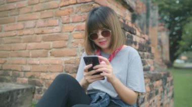 Gezgin Asyalı kadın sosyal medya ise Ayutthaya, Tayland tatil gezisi geçirdikten sonra dinlenmek, erkek zevk yolculuğunu geleneksel şehirde inanılmaz Simgesel Yapı itibariyle kontrol smartphone kullanarak. 
