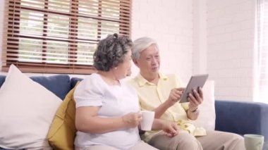 Tablet kullanma ve içme kahve evde oturma odasında Asya yaşlı çift çift evde rahat zaman kanepede yatarken aşk anın tadını çıkarın. Zaman yaşam tarzı üst düzey aile ev concept, zevk.