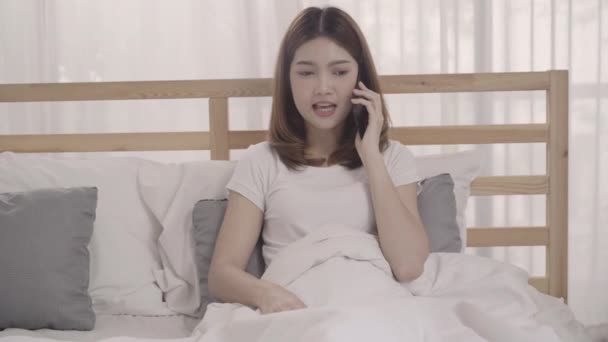 目を覚ます後ベッドの上に横たわっている間スマート フォンを使用して若いアジア女性笑顔美しい魅力的な日本人の女の子が自宅の寝室でリラックスします ホーム コンセプトでライフ スタイルの女性を時間を楽しんでください — ストック動画