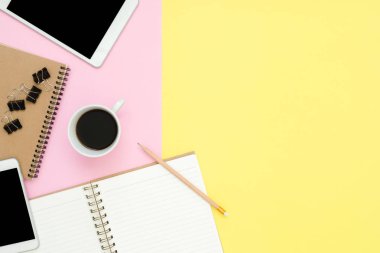 Ofis Masası adlı kullanıcının alanı - düz çalışma boş defter sayfası, kahve fincanı ve sahte telefon tablet pastel arka plan üzerinde yukarı çalışma alanının en iyi görünümü yatırın. Pastel pembe sarı renk arka plan boşluk kavramı.