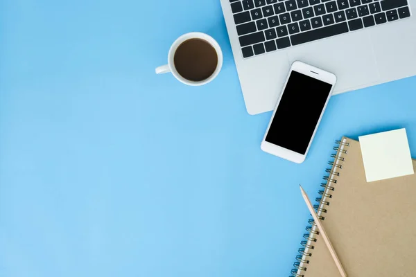 Office desk working space - Flat lay top view mockup photo of working space with laptop, smartphone, coffee and stationary on blue pastel background. Pastel blue color copy space working desk concept.