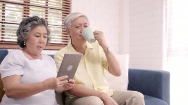 Tablet kullanma ve içme kahve evde oturma odasında Asya yaşlı çift çift evde rahat zaman kanepede yatarken aşk anın tadını çıkarın. Zaman yaşam tarzı üst düzey aile ev concept, zevk.