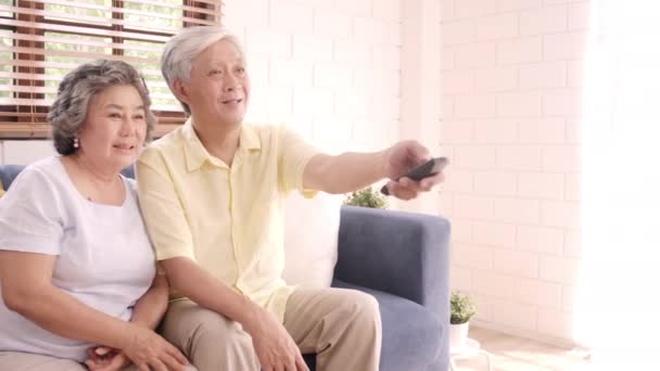 自宅のリビングルームでテレビを見ているアジアの高齢者のカップルは 甘いカップルが自宅でリラックスしたときにソファに横たわっている間 愛の瞬間をお楽しみください 家のコンセプトで時間ライフスタイルのシニア家族を楽しむ — ストック動画