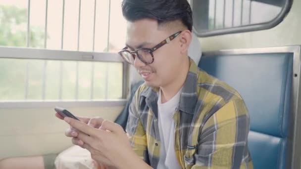 旅行者亚洲男子在乘坐火车时使用智能手机查看社交媒体 年轻的男性游客背包客享受她在泰国的旅程 生活方式青少年男子放松和旅行的概念 — 图库视频影像
