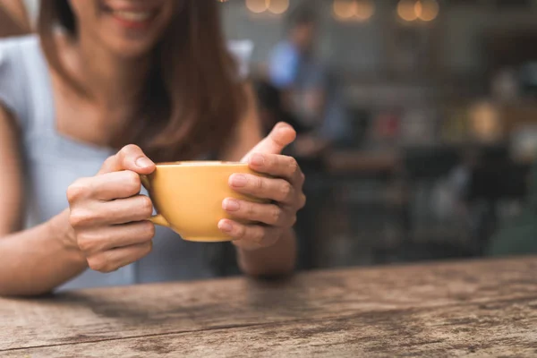 Cheerful asian young woman drinking warm coffee or tea enjoying it while sitting in cafe. Attractive happy asian woman holding a cup of coffee.