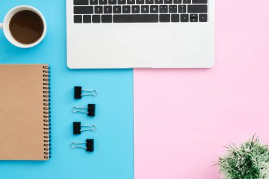 Yaratıcı düz Fotoğraf çalışma masası yatıyordu. Üstten görünüm ofis büro dizüstü bilgisayar, klip, defter, kahve fincanı ve bitki mavi pembe renkli arka plan üzerinde. Kopya alanı, düz yatıyordu fotoğraf ile üstten görünüm.