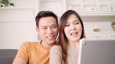 Asya çift evde oturma odasında arkadaşıyla Tablet Video seslenmek kullanma, tatlı çift evde rahat zaman kanepede yatarken aşk anın tadını çıkarın. Yaşam tarzı çift evde kavramı relax.