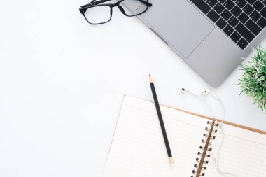 Yaratıcı düz Fotoğraf çalışma masası yatıyordu. Üstten görünüm ofis büro dizüstü bilgisayar, Gözlük, kalem, defter ve beyaz renk arka plan üzerinde bitki. Kopya alanı, düz yatıyordu fotoğraf ile üstten görünüm.