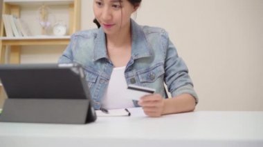 Evde oturma odasında masada oturma rahat giyirken kredi kartı ile online alışveriş satın tablet kullanarak güzel Asyalı kadın. Yaşam tarzı kadınlar evde çalışan konsept.