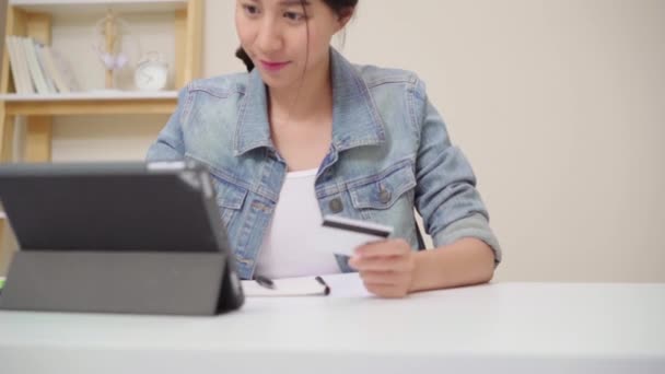 美丽的亚洲妇女使用平板电脑购买信用卡网上购物 而穿着休闲坐在办公桌上的客厅在家里 在家工作的生活方式妇女概念 — 图库视频影像