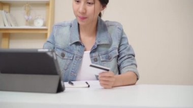 Evde oturma odasında masada oturma rahat giyirken kredi kartı ile online alışveriş satın tablet kullanarak güzel Asyalı kadın. Yaşam tarzı kadınlar evde çalışan konsept.