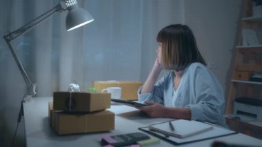 KOBİ 'nin genç Asya girişimci iş kadını sahibi online stokta ürün kontrol ve evde gece çalışma tablet kaydedin. Hasta ve yorgun hissediyorum. Ev ofisi konseptinde küçük işletme sahibi.
