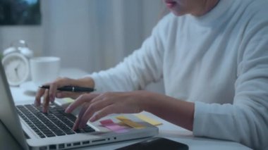Genç Asyalı kadın evde oturma odasında masada laptop kullanarak geç çalışma. Asya iş kadını ev ofisinde gece defter belge finans ve hesap yazma. Evde zaman zevk konsepti.