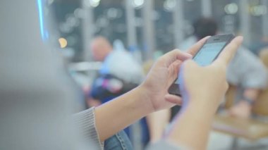 Kullanarak ve onun smartphone uçağının kalkış kapısı uluslararası havaalanında beklerken terminal Salonu sandalyede oturan süre kontrol mutlu Asyalı kadın. Kadınlar Havaalanı kavramında mutlu.