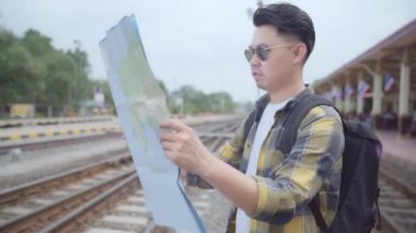 Seyahat Asya adam yön ve tatil gezi ve bekleyen tren tren istasyonunda harcama ise konumu harita üzerinde seyir, genç erkek turist backpacker yolculuk keyfini çıkarın. Yaşam tarzı erkekler kavramı seyahat.
