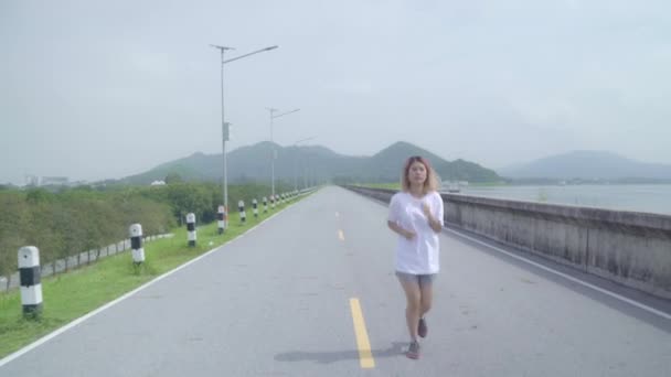 亚洲跑步女子在街头跑步和慢跑 健康美丽的年轻运动女性运动在湖边 生活方式适合和积极的妇女在街头的概念锻炼 — 图库视频影像