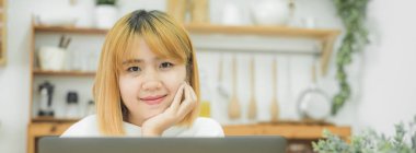 Evde oturma odasında otururken dizüstü bilgisayarda çalışma güzel genç gülümseyen Asyalı kadın. Ev ofisinde çalışan Asya iş kadın. Evde zaman zevk. Panoramik afiş.