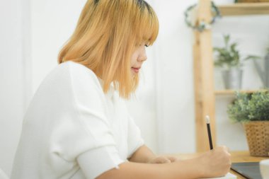 Evde oturma odasında otururken dizüstü bilgisayarda çalışma güzel genç gülümseyen Asyalı kadın. Ev ofisinde çalışan Asya iş kadın. Evde zaman zevk.