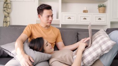 Asya çift evde oturma odasında arama web için dizüstü bilgisayar kullanarak, tatlı çift kanepede yatarken aşk keyfini ne zaman evde dinlenin. Yaşam tarzı çift evde kavramı relax.