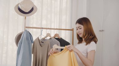 Evde dolap veya mağaza içinde onun moda kıyafet giysiler seçmek güzel çekici genç Asyalı kadın. Kız ne kazak giymeyi düşünüyorum. Ev dolap ya da soyunma giyim mağazası.