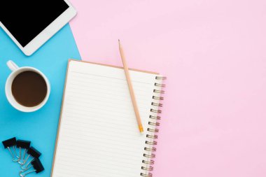 Yaratıcı düz fotoğraf çalışma masası yatıyordu. Üstten Görünüm Ofis Masası mavi pembe renkli arka plan üzerinde tablet, kalem, defter ve kahve Kupası ile. Kopya alanı, düz yatıyordu fotoğraf ile Üstten Görünüm.