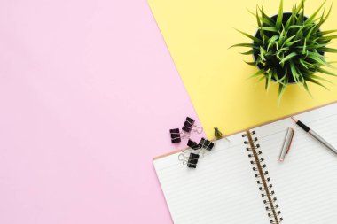 Yaratıcı düz fotoğraf çalışma masası yatıyordu. Üstten Görünüm Ofis Masası ile defter ve kalem ve bitki pembe sarı pastel renk arka plan üzerine açık sahte. Kopya alanı, düz yatıyordu fotoğraf ile Üstten Görünüm.