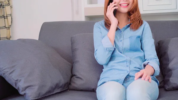 Retrato de belo atraente jovem sorridente mulher asiática falando no telefone inteligente com os amigos enquanto deitado no sofá quando relaxar na sala de estar em casa. Desfrutando de tempo estilo de vida mulheres em casa conceito . — Fotografia de Stock