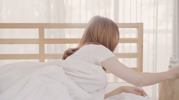 Vakker, ung asiatisk kvinne våkner og smiler og strekker armene i sengen sin på soverommet. Ung asiatisk kvinne bruker avslapningstid hjemme. Livsstilskvinner som bruker avslapningstid hjemme-konseptet . – stockfoto
