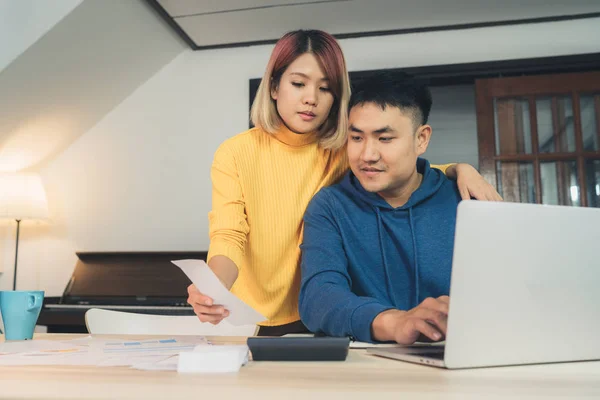 Jovem casal asiático gerenciando finanças, revisando suas contas bancárias usando computador portátil e calculadora em casa moderna. Mulher e homem fazendo papelada juntos, pagando impostos on-line no notebook pc . — Fotografia de Stock