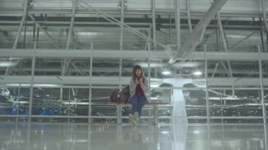 Kullanarak ve onun smartphone uçağının kalkış kapısı uluslararası havaalanında beklerken terminal Salonu sandalyede oturan süre kontrol mutlu Asyalı kadın. Kadınlar Havaalanı kavramında mutlu.