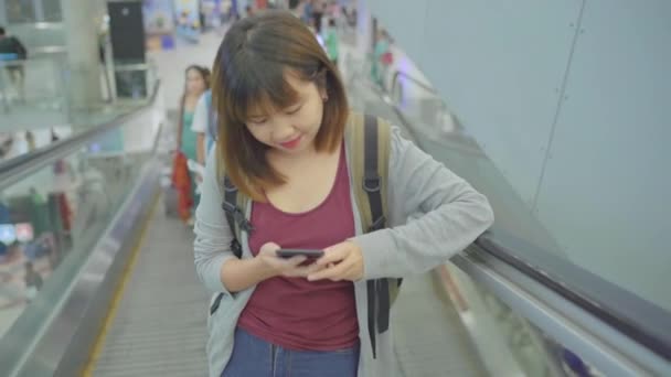 愉快的亚洲妇女使用和检查她的智能手机在候机楼大厅 而等待她的航班在国际机场的登机口 妇女高兴在机场概念 — 图库视频影像