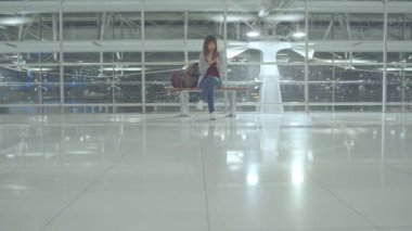 Kullanarak ve onun smartphone uçağının kalkış kapısı uluslararası havaalanında beklerken terminal Salonu sandalyede oturan süre kontrol mutlu Asyalı kadın. Kadınlar Havaalanı kavramında mutlu.