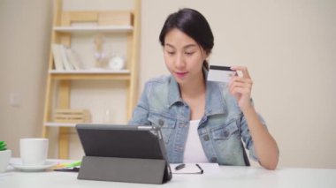 Evde oturma odasında masada oturma rahat giyirken kredi kartı ile online alışveriş satın tablet kullanarak güzel Asyalı kadın. Yaşam tarzı kadınlar evde çalışan konsept.