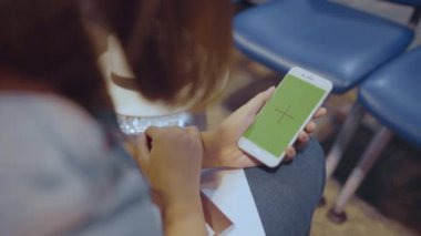 Asyalı kadın uçağının kalkış kapısı uluslararası havaalanında beklerken terminal salonunda yeşil ekran beyaz hareket eden telefon aygıt kullanarak. Kadınlar Havaalanı kavramında mutlu. Chroma anahtar.