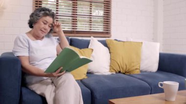 Asyalı yaşlı kadın evde oturma odasında bir kitap okuyor. Çinli kadın evde rahat zaman kanepede yatıyor. Evde kavramı zaman yaşam tarzı kıdemli kadın zevk.