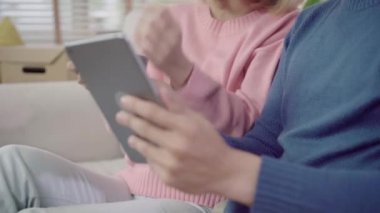 Tablet kullanan ve evde oturma odasında kahve içen genç Asyalı çift, evde rahatken kanepede yatarken aşk anının tadını çıkarıyor. Evde konseptte zaman yaşam tarzı ailesinin keyfini çıkarın.