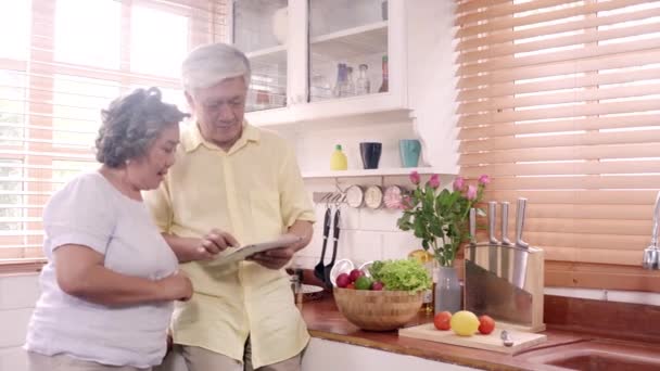 亚洲老年夫妇使用片剂准备原料在厨房制作食物 夫妇使用有机蔬菜在家里的健康食品 生活方式 老年家庭在家做食物的概念 — 图库视频影像
