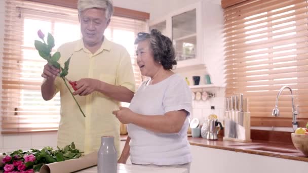 アジアの高齢夫婦が自宅の台所の木製のテーブルに花束を作る 時間を使った中国の甘いシニアカップルは 自宅で一緒にリラックスします 家庭コンセプトのライフスタイルシニアカップル — ストック動画